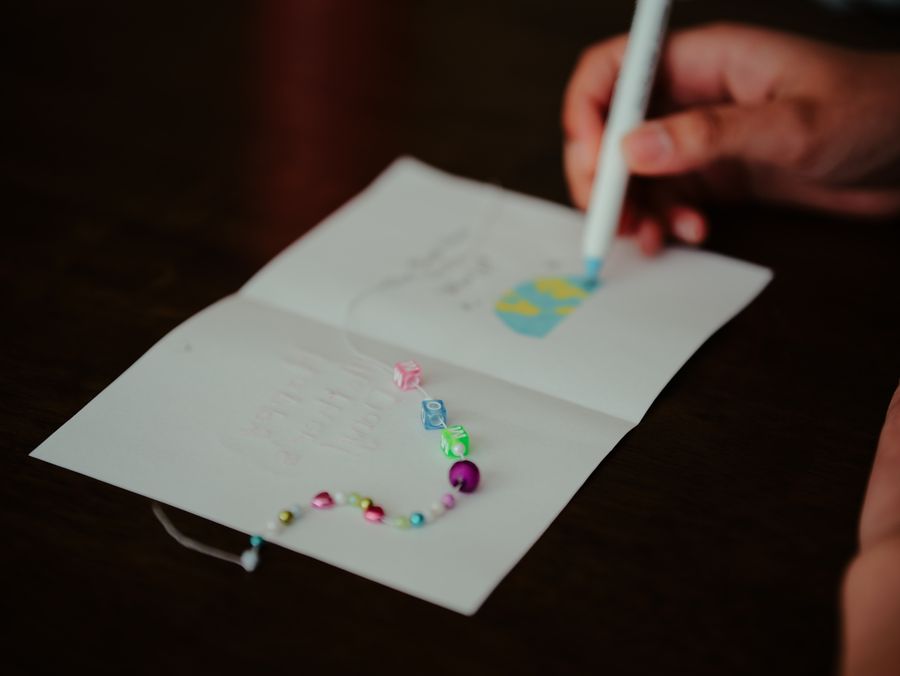 Een hand plaatst met een pen kleine gekleurde steentjes in een boog op een opengeslagen kaart.